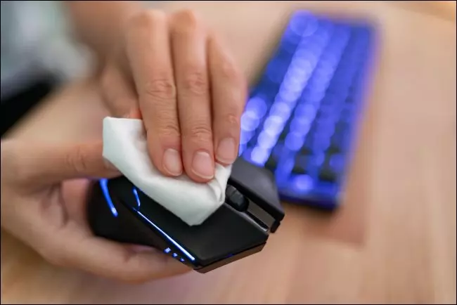 Рука, вытирающая компьютерную мышь тканью.